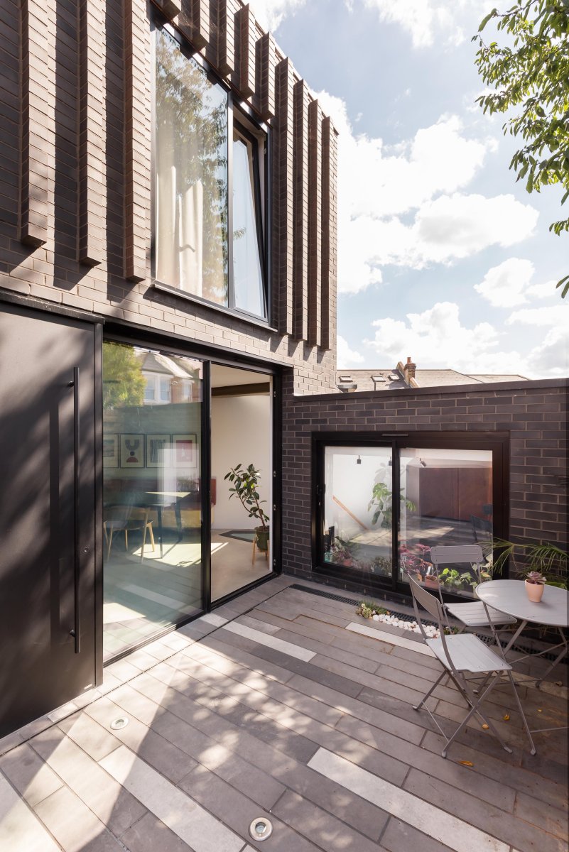 Front elevation of a contemporary new-build house in Forest Hill, featuring black brickwork, large glazed doors and a paved courtyard.