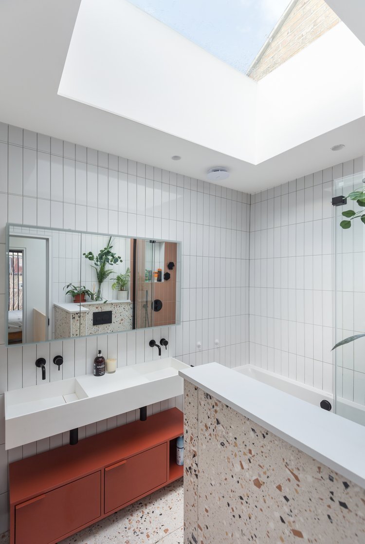 Contemporary bathroom with a large rooflight, white wall tiles, terrazzo bath surround and terracotta-coloured vanity.