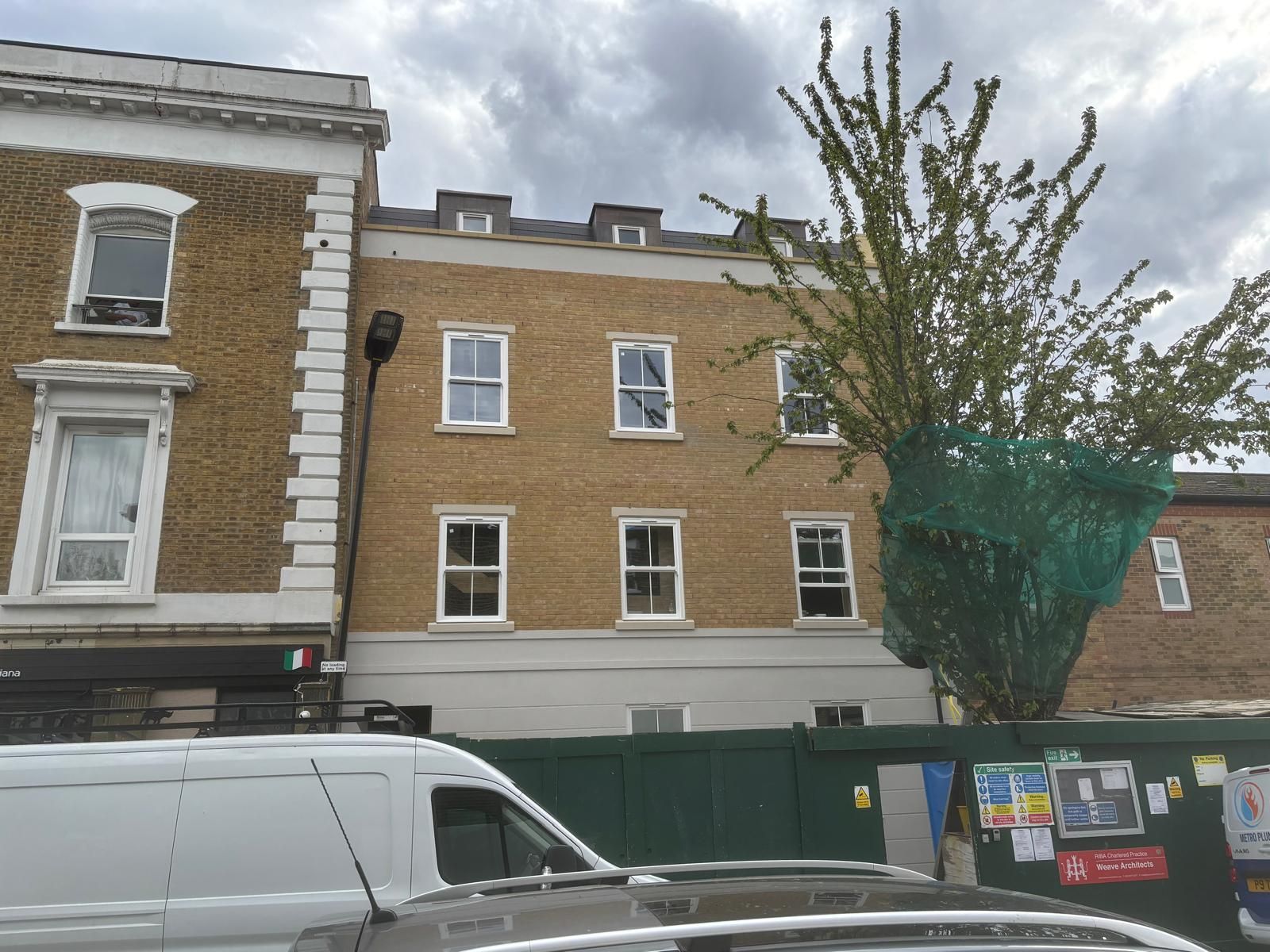 Front elevation of a new-build apartment development in Hackney, with yellow brickwork, white-framed windows