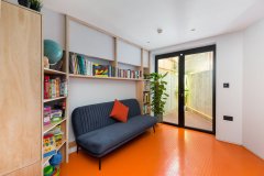 Living space with orange flooring, built-in timber shelving and glazed doors in a new-build house in Forest Hill.
