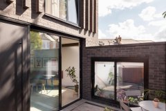 Front elevation of a contemporary new-build house in Forest Hill, featuring black brickwork, large glazed doors and a paved courtyard.