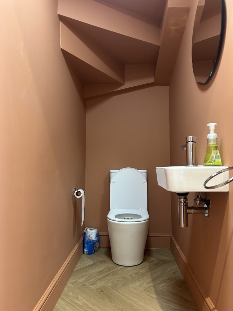 Downstairs cloakroom with terracotta-coloured walls, compact wall-mounted basin and herringbone flooring at Massingberd Way, Tooting.