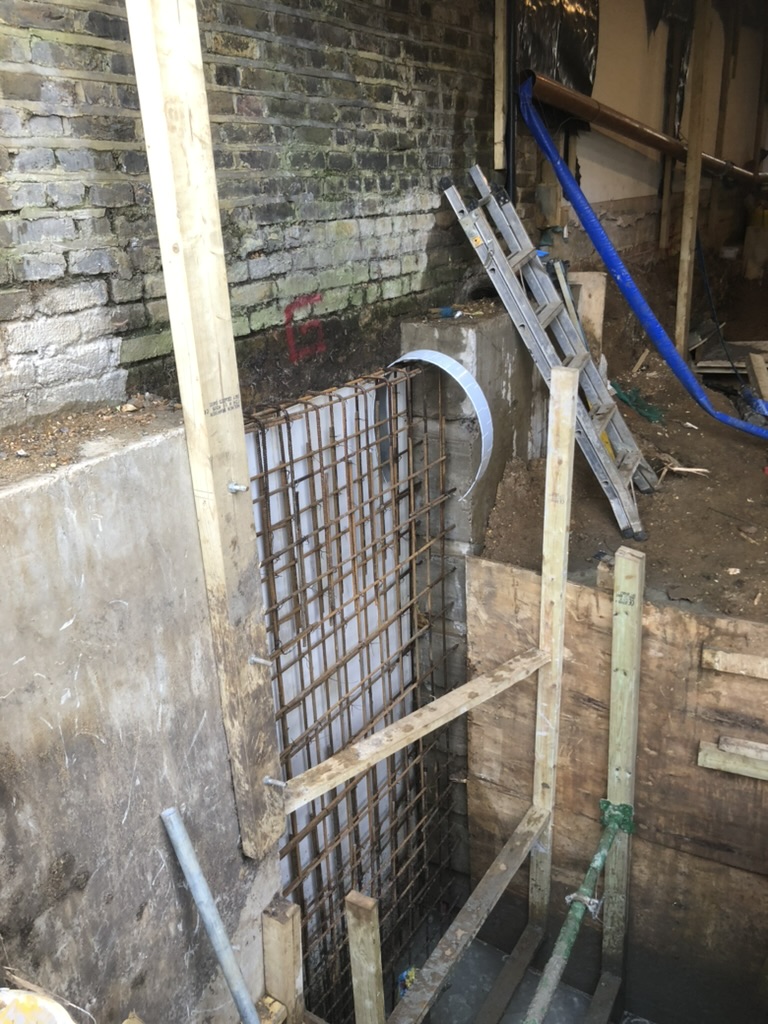 Rebar and shuttering for the next basement retaining wall section next to a completed bay