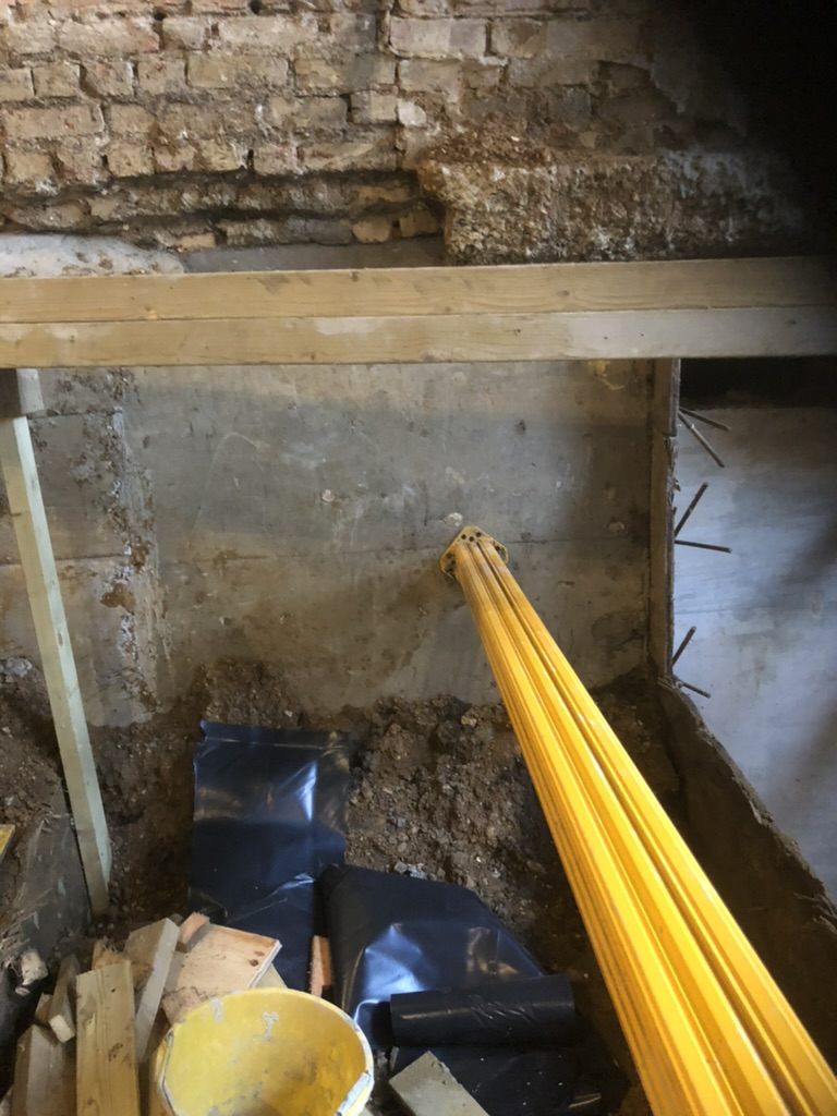 Hydraulic prop bracing a finished underpinning section during the basement excavation