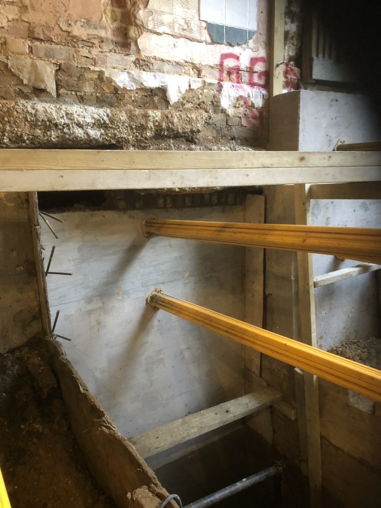 Completed concrete underpinning bay beneath the original brick footing, propped while the next bay is excavated