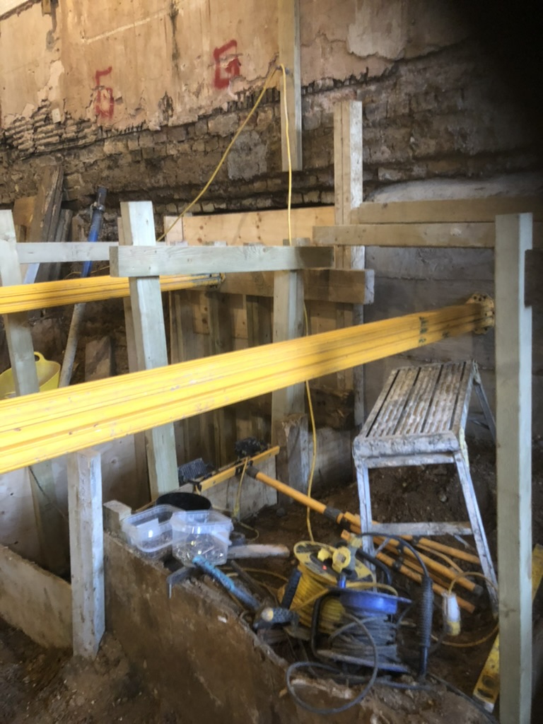 Underpinning bays under the existing Victorian wall, held by hydraulic props and timber walings during the basement dig at Edna Street, Battersea