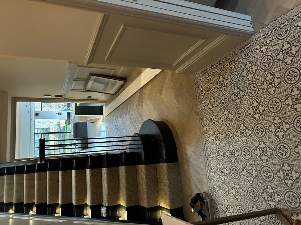 Widened Victorian hallway with patterned floor tiles, herringbone oak, panelled walls and an ebonised staircase with curtail step